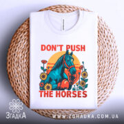 Футболка жарт і стиль. Біла футболка з принтом, на якому зображений кінь у рукавичках, оточений квітами на фоні сонця. Футболка складена на плетеному кошику, фон світлий.