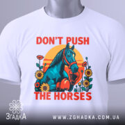 Футболка жарт і стиль. Біла футболка з принтом, на якому зображений кінь у рукавичках, оточений квітами на фоні сонця. Футболка складена на столі, з прикріпленою етикеткою, фон світлий, з легким градієнтом.