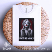 Футболка жінка тату білого кольору, зображена на плетеній тарілці, фон світлий, принт з чорно-білою жінкою з червоними губами та татуюваннями, текст "ВЖЕ НЕ МОЖУ" під зображенням.