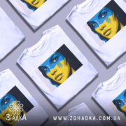 Футболка жінка Україна, біла, зображена на манекені, фон градієнтний сірий, принт з обличчям жінки з синьо-жовтим малюнком на обличчі та гербом України.