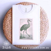 Футболка журавель стиль, біла футболка, складена на плетеній кошику, з принтом журавля, фон світло-сірий, принт оформлений у вигляді поштової марки.