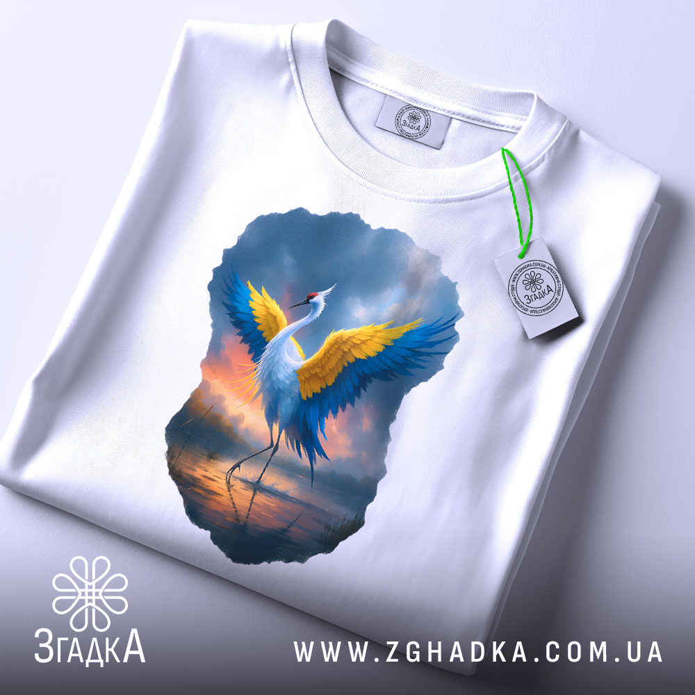 Футболка журавель України, біла, зображена зверху, на фоні світло-сірого, принт з журавлем з жовтими і блакитними крилами, прикріплений етикеткою з зеленим шнурком.