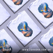 Футболка журавель України, біла, зображена з фронтального ракурсу, на фоні світло-сірого градієнту, принт з журавлем з розпростертими жовтими і блакитними крилами на фоні заходу сонця.