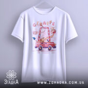 Футболка жираф у машині, біла, підвішена на вішалці, фон світло-сірий, принт з жирафом у червоній машині, яскраві кольори.