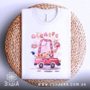 Футболка жираф у машині, біла, лежить на плетеній кошику, фон світло-сірий, принт з жирафом у червоній машині, деталі принта яскраві та веселкові.