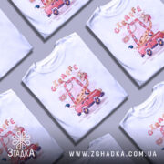 Футболка жираф у машині, біла, зображена на манекені, фон світло-сірий, принт з жирафом у червоній машині з веселими деталями.