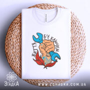 Футболка життя б`є ключем. Біла футболка складена на плетеній основі, принт з рукою, що тримає синій ключ, оточений червоними листям, чітко видимий. Фон світлий.