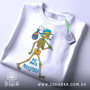 Футболка життя мандрівка, біла, зображена зверху, на фоні світлого градієнту, принт з малюнком скелета, який йде з мішком, текст "ВСЕ ЖИТТЯ МАНДРІВКА" внизу, з етикеткою на рукаві.