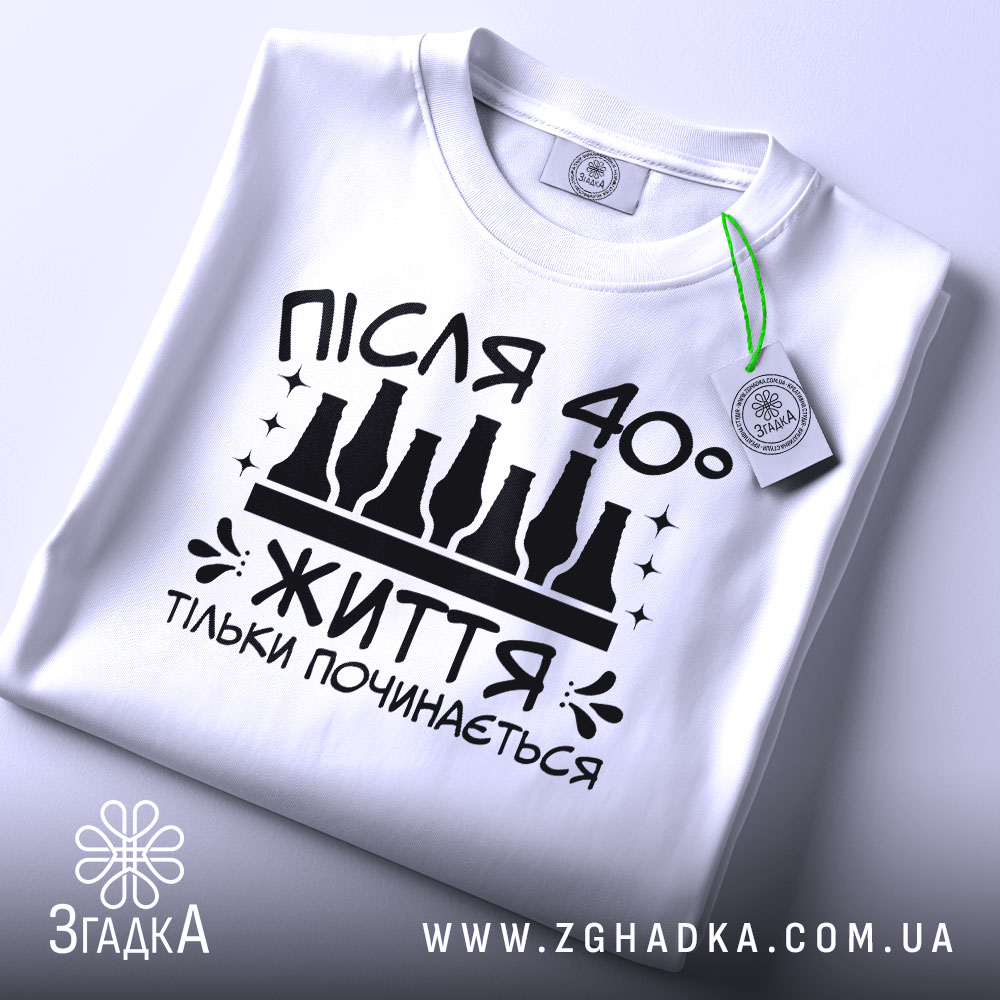 Футболка життя після 40, білого кольору, зображена зверху, на ній видно етикетку з зеленим шнурком, фон світлий, принт чорного кольору з написом 'ПІСЛЯ 40° ЖИТТЯ ТІЛЬКИ ПОЧИНАЄТЬСЯ' та пляшками.