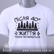 Футболка життя після 40, білого кольору, зображена зверху, на ній видно етикетку з зеленим шнурком, фон світлий, принт чорного кольору з написом 'ПІСЛЯ 40° ЖИТТЯ ТІЛЬКИ ПОЧИНАЄТЬСЯ' та пляшками.