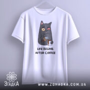 Футболка життя після кави, білого кольору, підвішена на вішалці, фон світлий, принт з котом, що п'є каву, з виразом обличчя, що показує емоції, текст під принтом чорного кольору.