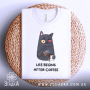 Футболка життя після кави, складена на плетеній кошику, фон світлий, принт з котом, що п'є каву, з виразом обличчя, що показує емоції, текст під принтом чорного кольору.