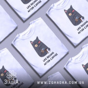 Футболка життя після кави, білого кольору, зображена на манекені з металевим блиском, фон нейтральний, принт з котом, що п'є каву, з виразом обличчя, що показує емоції, текст під принтом чорного кольору.