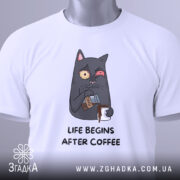 Футболка життя після кави, складена на поверхні, з видимим етикеткою, фон світлий, принт з котом, що п'є каву, з виразом обличчя, що показує емоції, текст під принтом чорного кольору.