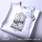 Футболка життя це подорож. Біла футболка, складена на поверхні, з видимим принтом чорного кольору. На футболці напис "Життя це подорож, а не пункт призначення" у стилі ретро, з етикеткою зеленого кольору, фон світло-сірий.