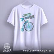 Футболка життя це подорож, біла футболка підвішена на вішалці, з принтом велосипеда, фон світло-сірий, принт виконаний у блакитному та жовтому кольорах.
