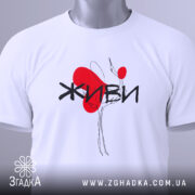 Футболка живи білого кольору, складена на плоскій поверхні, фон світло-сірий, принт з червоним серцем та чорним написом 'ЖИВИ', на комірці видна етикетка.