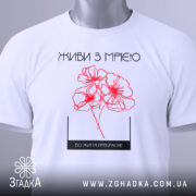 Футболка живи з мрією, білого кольору, складена на поверхні, фон світлий, принт з червоними квітами та написом, на футболці є етикетка.