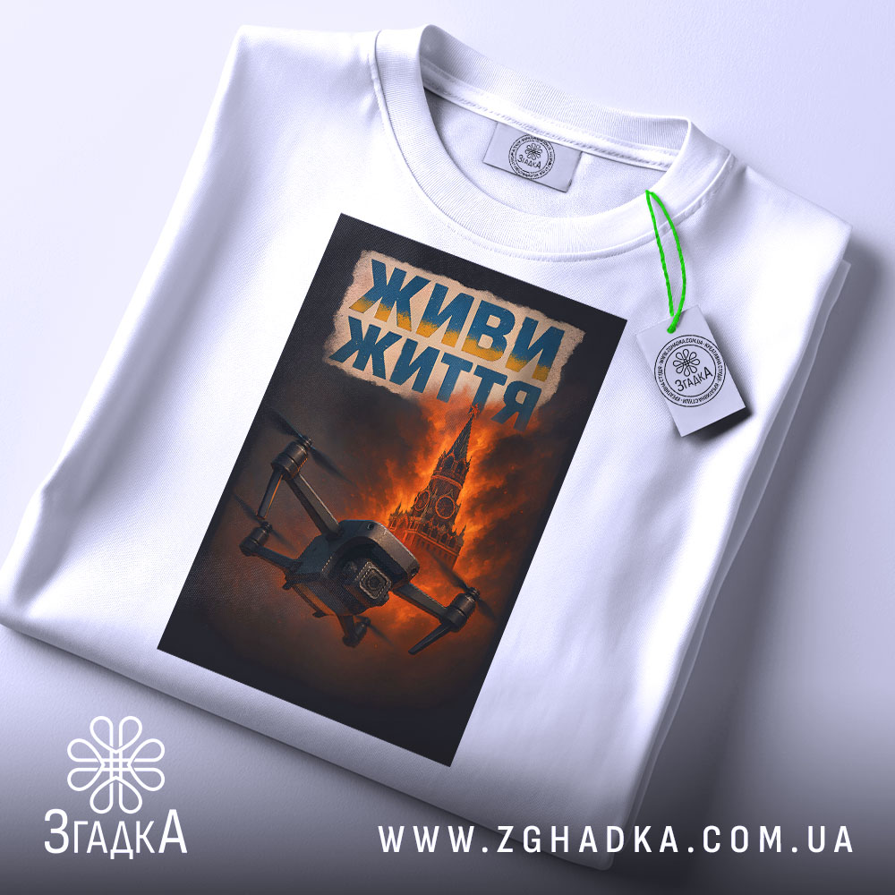 Футболка живи життя дрон, біла, складена на поверхні, фон світло-сірий, принт з дроном на фоні червоного неба та Кремлівської вежі, текст 'ЖИВИ ЖИТТЯ' у верхній частині принта, з етикеткою на комірці.
