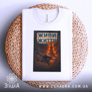 Футболка живи життя дрон, біла, складена на плетеній основі, фон світло-сірий, принт з дроном на фоні червоного неба та Кремлівської вежі, текст 'ЖИВИ ЖИТТЯ' у верхній частині принта.