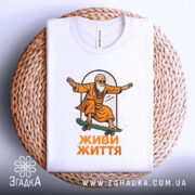 Футболка живи життя, біла, зображена в складеному вигляді на плетеній основі, на фоні світло-сірого градієнту, принт з малюнком старця на скейтборді в оранжевому одязі, текст 'ЖИВИ ЖИТТЯ' під малюнком.