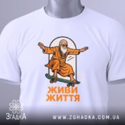 Футболка живи життя, біла, зображена в складеному вигляді, на фоні світло-сірого градієнту, принт з малюнком старця на скейтборді в оранжевому одязі, текст 'ЖИВИ ЖИТТЯ' під малюнком, на етикетці зелена стрічка.
