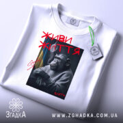 Футболка живи життя, біла, складена на поверхні, з принтом шимпанзе, що курить, з червоним написом 'ЖИВИ ЖИТТЯ' та тегом на зеленій стрічці.