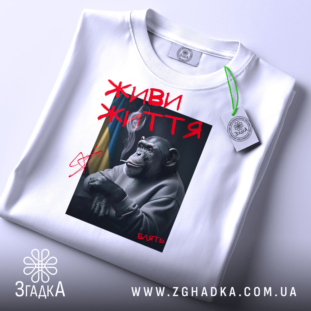 Футболка живи життя, біла, складена на поверхні, з принтом шимпанзе, що курить, з червоним написом 'ЖИВИ ЖИТТЯ' та тегом на зеленій стрічці.