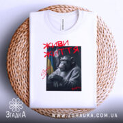 Футболка живи життя, біла, складена на кошику, з принтом шимпанзе, що курить, червоний напис 'ЖИВИ ЖИТТЯ', фон світлий.