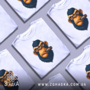 Футболка зла мавпа, біла, зображена на манекені, фон світло-сірий, принт з обличчям мавпи з сигарою, деталі принта яскраві та контрастні.