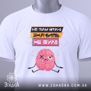 Футболка значить не було. Біла футболка, складена на поверхні, з принтом мозку, який виглядає сумно. Текст на футболці: 'НЕ ПАМ'ЯТЮ ЗНАЧИТЬ НЕ БУЛО'. На футболці є етикетка з зеленим шнурком. Фон світлий, з легким відблиском.