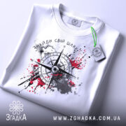 Футболка знайди свій шлях, біла, розкладена на поверхні, фон світло-сірий, принт з компасом, зелена етикетка.