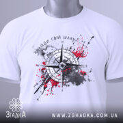 Футболка знайди свій шлях, біла, розкладена на поверхні, фон світло-сірий, принт з компасом, зелена етикетка.