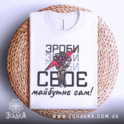 Футболка зроби сам, білого кольору, зображена зверху на плетеній кошику, фон світло-сірий, принт аналогічний попереднім, текст чорного кольору.