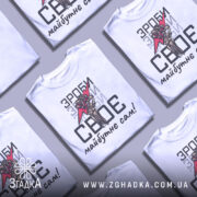 Футболка зроби сам, білого кольору, зображена з фронтального ракурсу на манекені, фон світло-сірий, принт містить червоний блискавку та малюнок руки, що тримає її, текст чорного кольору.