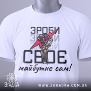 Футболка зроби сам, білого кольору, зображена зверху, на ній видно етикетку з зеленим шнурком, фон світло-сірий, принт аналогічний попередньому, текст чорного кольору.