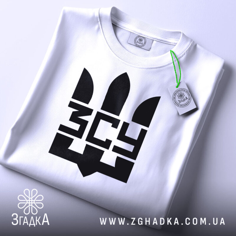 Футболка ЗСУ білого кольору, зображена зверху, складена на столі, фон світло-сірий, принт чорного кольору з тризубом та написом 'ЗСУ', на комірці є етикетка з зеленим шнурком.