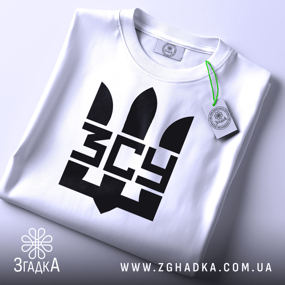 Футболка ЗСУ білого кольору, зображена зверху, складена на столі, фон світло-сірий, принт чорного кольору з тризубом та написом 'ЗСУ', на комірці є етикетка з зеленим шнурком.
