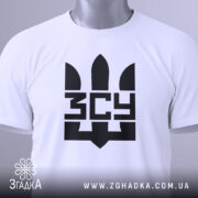 Футболка ЗСУ білого кольору, зображена зверху, складена на столі, фон світло-сірий, принт чорного кольору з тризубом та написом 'ЗСУ', на комірці є етикетка з зеленим шнурком.