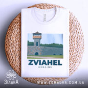 Футболка Звягель місто, біла, складена на плетеній кошику, фон світлий, принт з малюнком вежі на кам'яній стіні з написом ZVIAHEL UKRAINE.