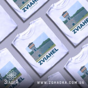 Футболка Звягель місто, біла, зображена на манекені, фон нейтральний, принт з малюнком вежі на кам'яній стіні з написом ZVIAHEL UKRAINE.
