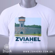 Футболка Звягель місто, біла, складена на столі, фон світлий, принт з малюнком вежі на кам'яній стіні з написом ZVIAHEL UKRAINE, на футболці є етикетка з зеленим шнурком.