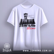 Футболка Звягель білого кольору, зображена на манекені, з принтом, що містить вежу та дерева, текст виконаний чорним і червоним кольорами, фон світло-сірий.