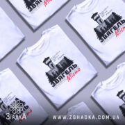 Футболка Звягель білого кольору, зображена на манекені, з принтом, що містить вежу та дерева, текст виконаний чорним і червоним кольорами, фон світло-сірий.