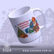 Горнятко для слухняної дівчинки, біле, зображене з легким нахилом на світлому фоні, на ньому принт з різдвяною ялинкою, подарунками та персонажем у червоній шапці, ручка гладка, край рівний, глянець на поверхні.