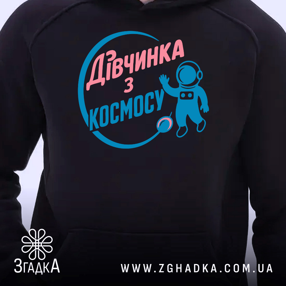 Худі дівчинка з космосу. Темно-синій худі з близького ракурсу, на якому видно принт з текстом та малюнком космонавта. Капюшон піднятий, фон світлий, акцент на деталях принта та манжетах.