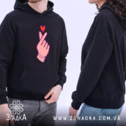 Худі finger heart дизайн, чорного кольору, на моделі, з капюшоном, з кишенею-«кенгуру», принт у вигляді руки з серцем видно з обох боків, манжети та пояс виконані в класичному стилі.