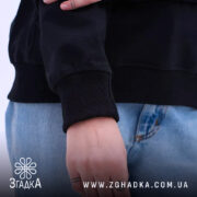 Худі finger heart дизайн, чорного кольору, з акцентом на манжетах, які щільно прилягають, рука моделі на кишені, видно текстуру матеріалу, що підкреслює стиль.