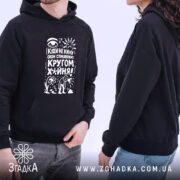 Худі кругом х*йня, чорного кольору, з капюшоном, з бокового ракурсу, на фоні світлого кольору, з принтом на грудях, що містить текст і малюнки, на моделі чоловіка та жінки.