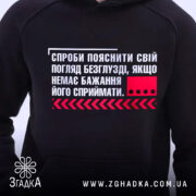 Худі пояснити погляд. Чорний колір, ракурс спереду, фон світлий. Принт на грудях з текстом та червоним квадратом, кишеня-«кенгуру» присутня, капюшон ззаду, манжети та пояс виконані в еластичному матеріалі.